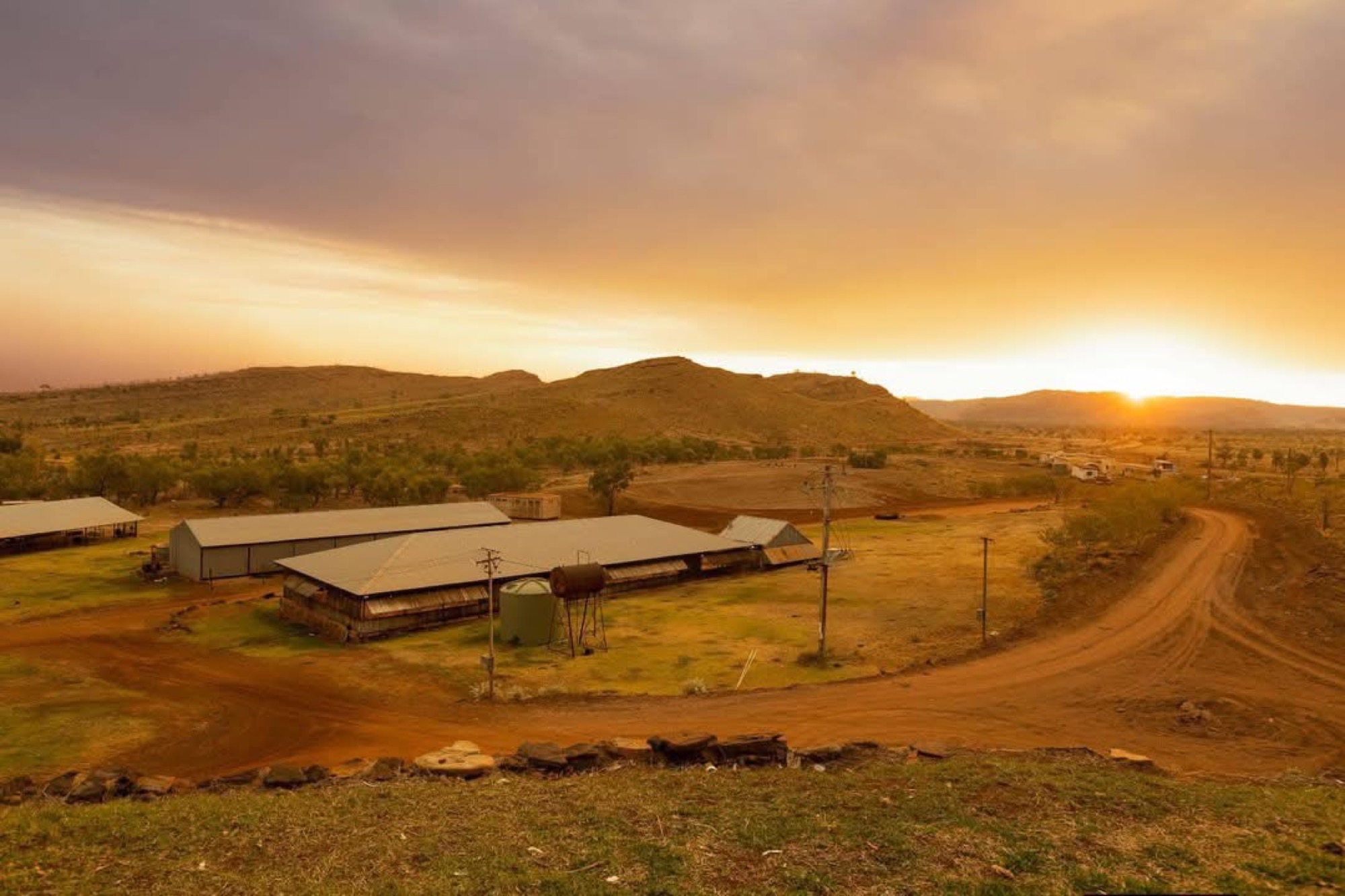 Golden sunset over a remote outback station with red dirt road and mountain backdrop