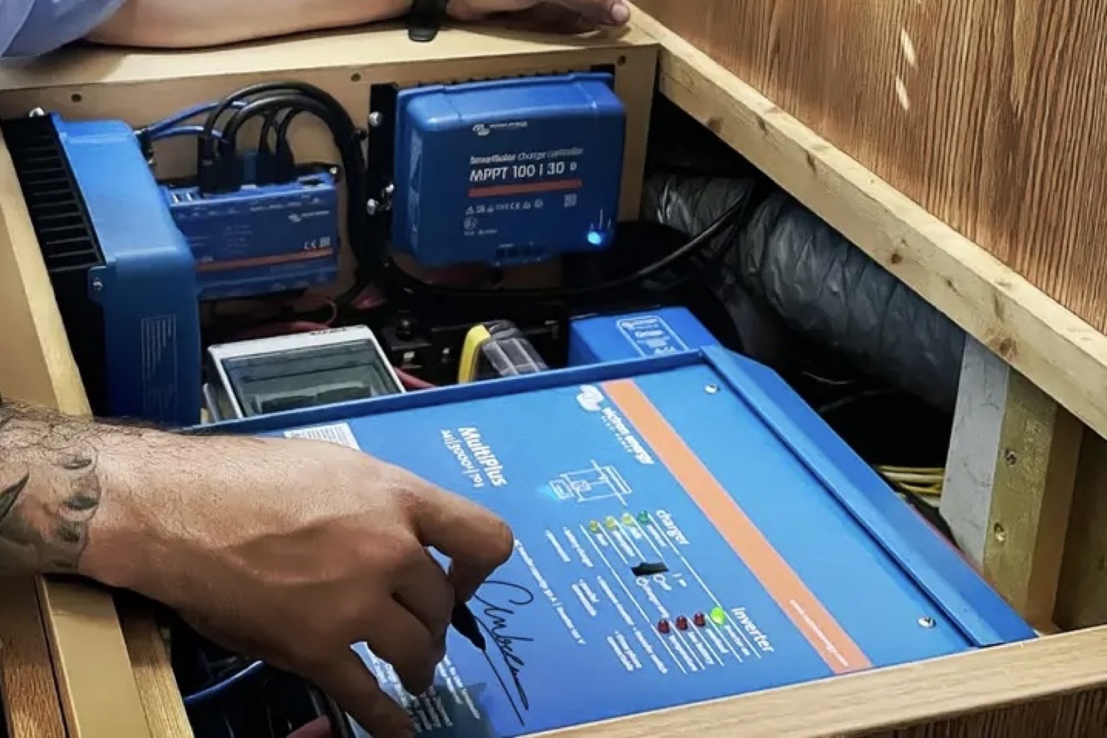 Tattooed hands installing Victron MultiPlus in a timber enclosure