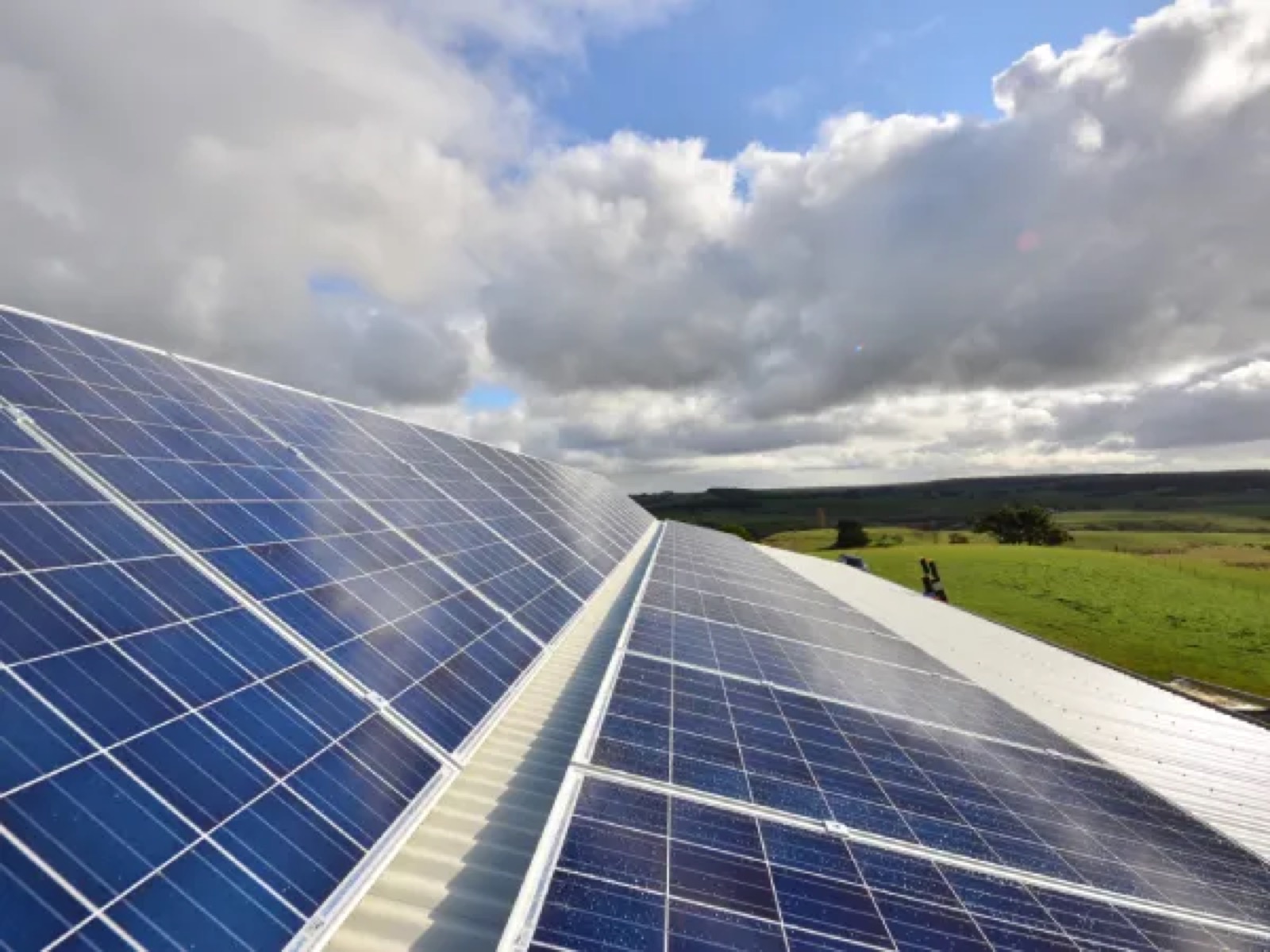 Solar panels sweeping across a rooftop against open sky and green paddocks